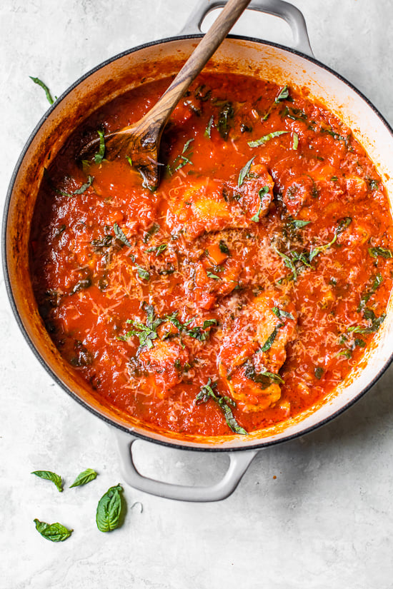 Chicken cacciatore is a rustic Italian chicken dish made with bell peppers and mushrooms slow-simmered in a rich tomato sauce with herbs. Overhead view of classic chicken cacciatore with peppers and tomatoes in a Dutch oven.