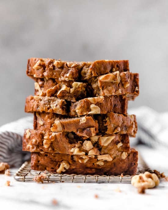 This delicious banana bread is be made with ripe mashed bananas, nuts, and spices. It's made healthier with less butter, oil and sugar. Slices of banana nut bread stacked on a wire rack.