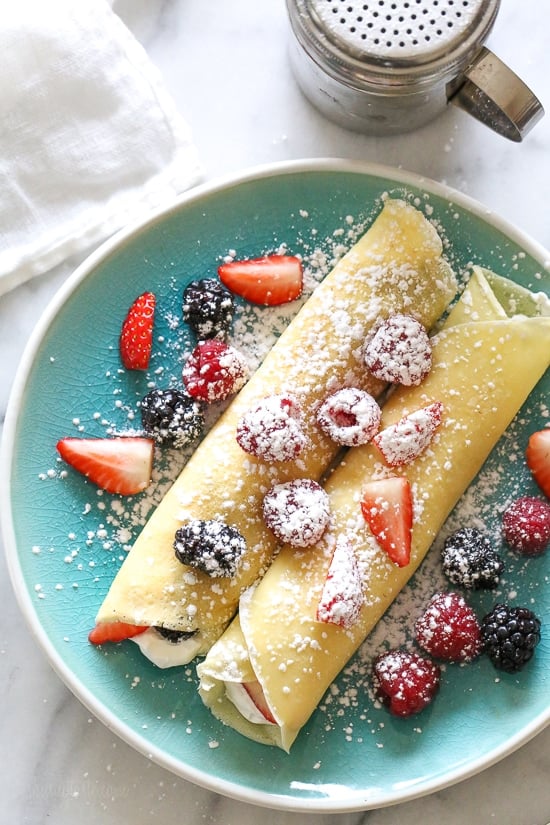 With just 4 main ingredients and everything prepared in the blend, this Easy Crepes Recipe is virtually foolproof! Homemade crepes with whipped cream and fresh berries on a blue plate