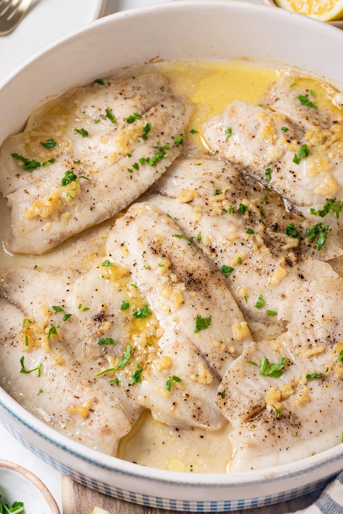 This simple baked tilapia recipe is finished with a garlicky lemon butter sauce and parsley, making it a delicious and light weeknight dinner! Healthy baked tilapia in pan
