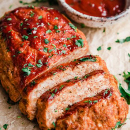 Turkey meatloaf cut into slices next to a bowl of ketchup glaze.
