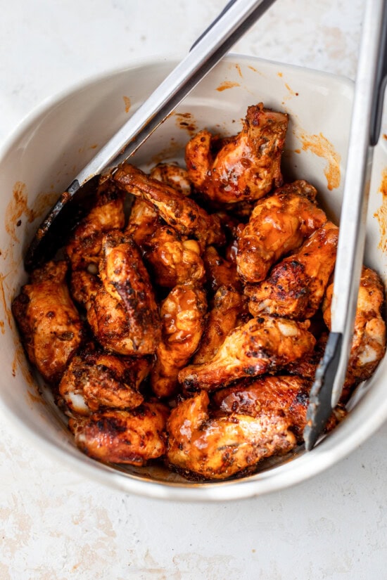 These homemade buffalo wings will be the hit at your next football party! They're baked in the oven and so much lighter than deep-fried. Buffalo chicken wings tossed in buffalo sauce in a bowl with tongs.