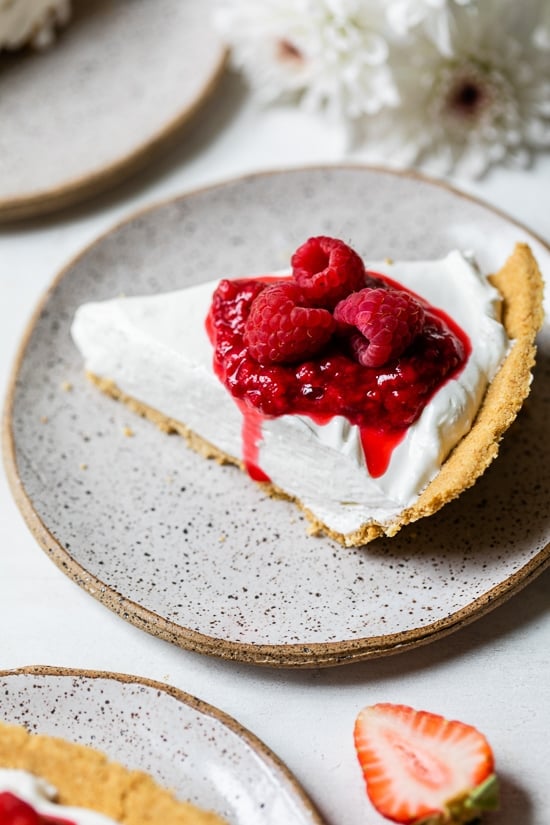 This easy no-bake cheesecake is light, dreamy and so easy to make, you don’t even need an oven. A little slice of heaven! Slice of creamy no-bake cheesecake topped with macerated and fresh raspberries