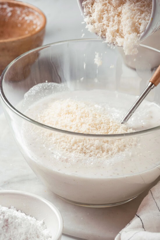 These homemade coconut popsicles are rich, creamy, and super simple to make! They’re the perfect summertime refresher. Adding shredded coconut to popsicle mixture in bowl