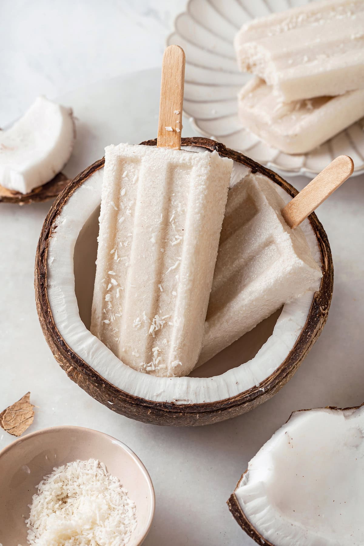 These homemade coconut popsicles are rich, creamy, and super simple to make! They’re the perfect summertime refresher. Two coconut popsicles set in halved coconut
