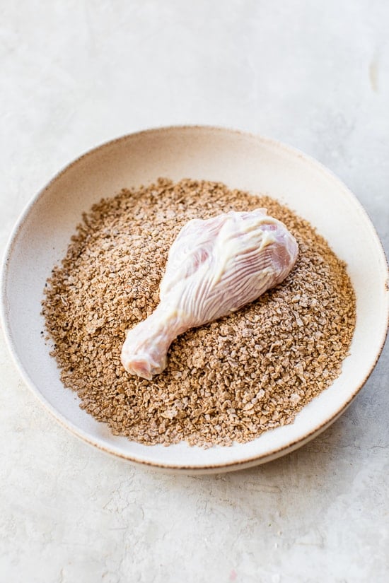 This healthy oven fried chicken is moist on the inside, golden and extra crispy on the outside thanks to a secret ingredient: bran flakes! Chicken drumstick in bowl of bran flake coating.