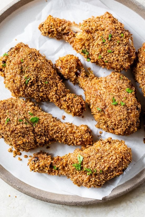 This healthy oven fried chicken is moist on the inside, golden and extra crispy on the outside thanks to a secret ingredient: bran flakes! Oven fried chicken on parchment lined plate.