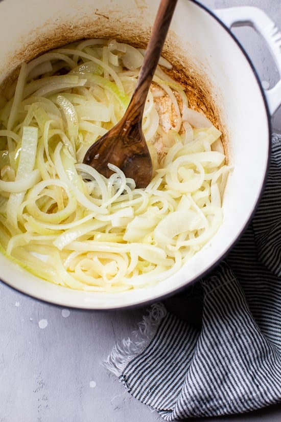 This lightened-up French onion soup recipe is just as delicious as the original, with beefy broth, caramelized onions, and melty cheese! Sliced onions being stirred in a pot by a wooden spoon.