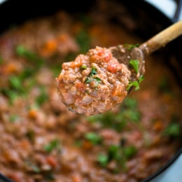 A spoonful of bolognese sauce held over a pot of sauce.