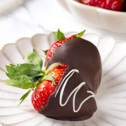 Two chocolate-covered strawberries on white plate