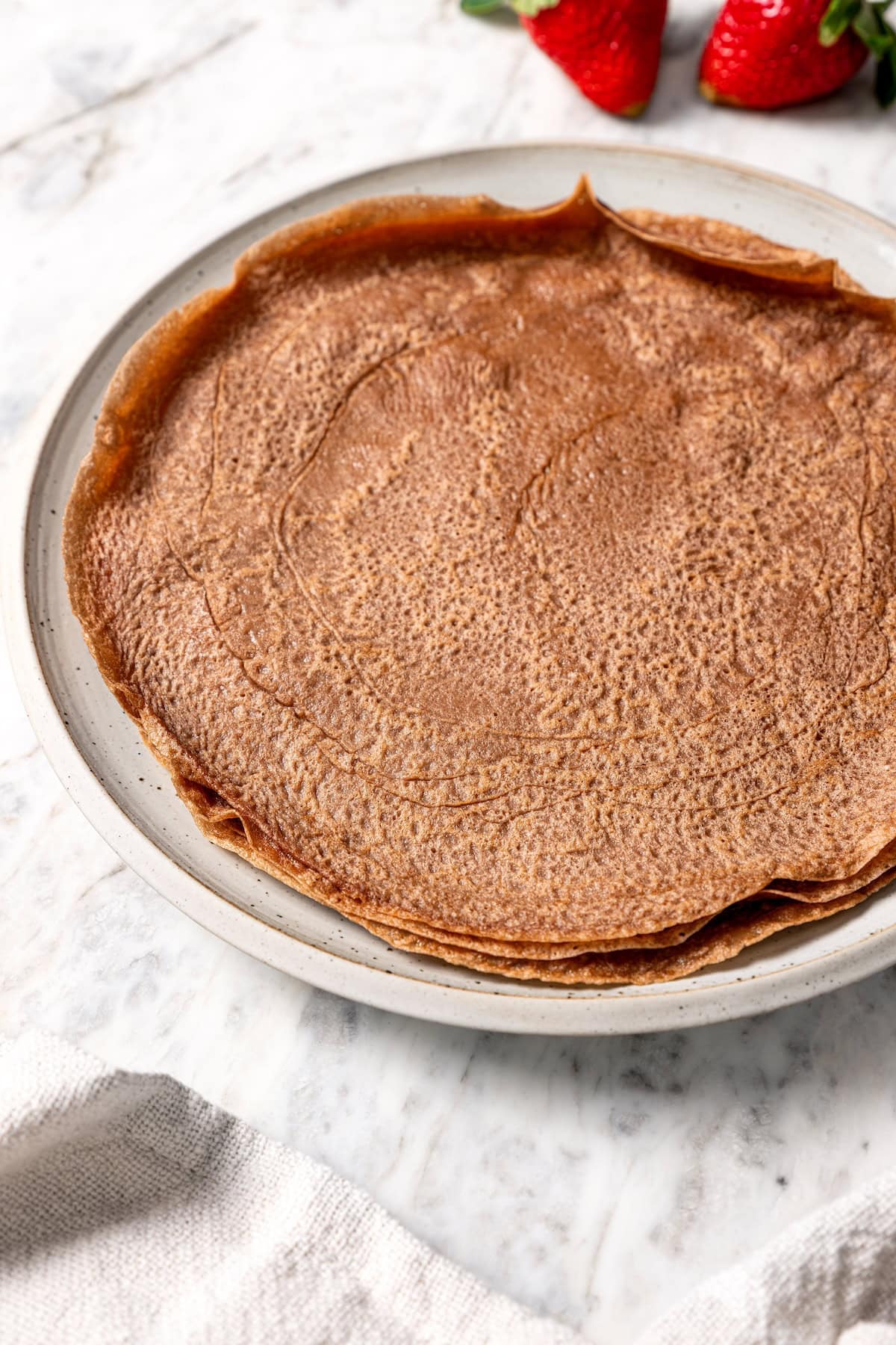 These chocolate crepes are thin, tender and lightly sweet, filled with strawberries and whipped topping. Serve them for breakfast or dessert! Stack of chocolate crepes on plate.
