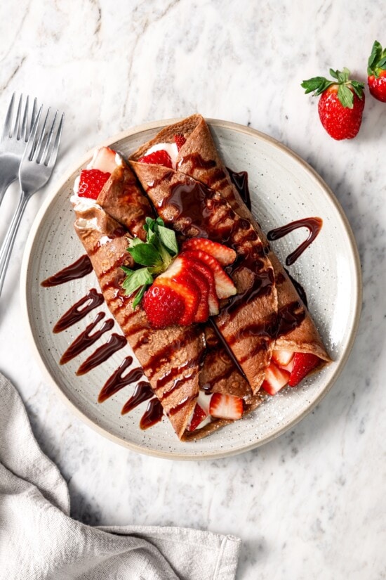 These chocolate crepes are thin, tender and lightly sweet, filled with strawberries and whipped topping. Serve them for breakfast or dessert! Plate of chocolate crepes with Cool Whip and strawberries.