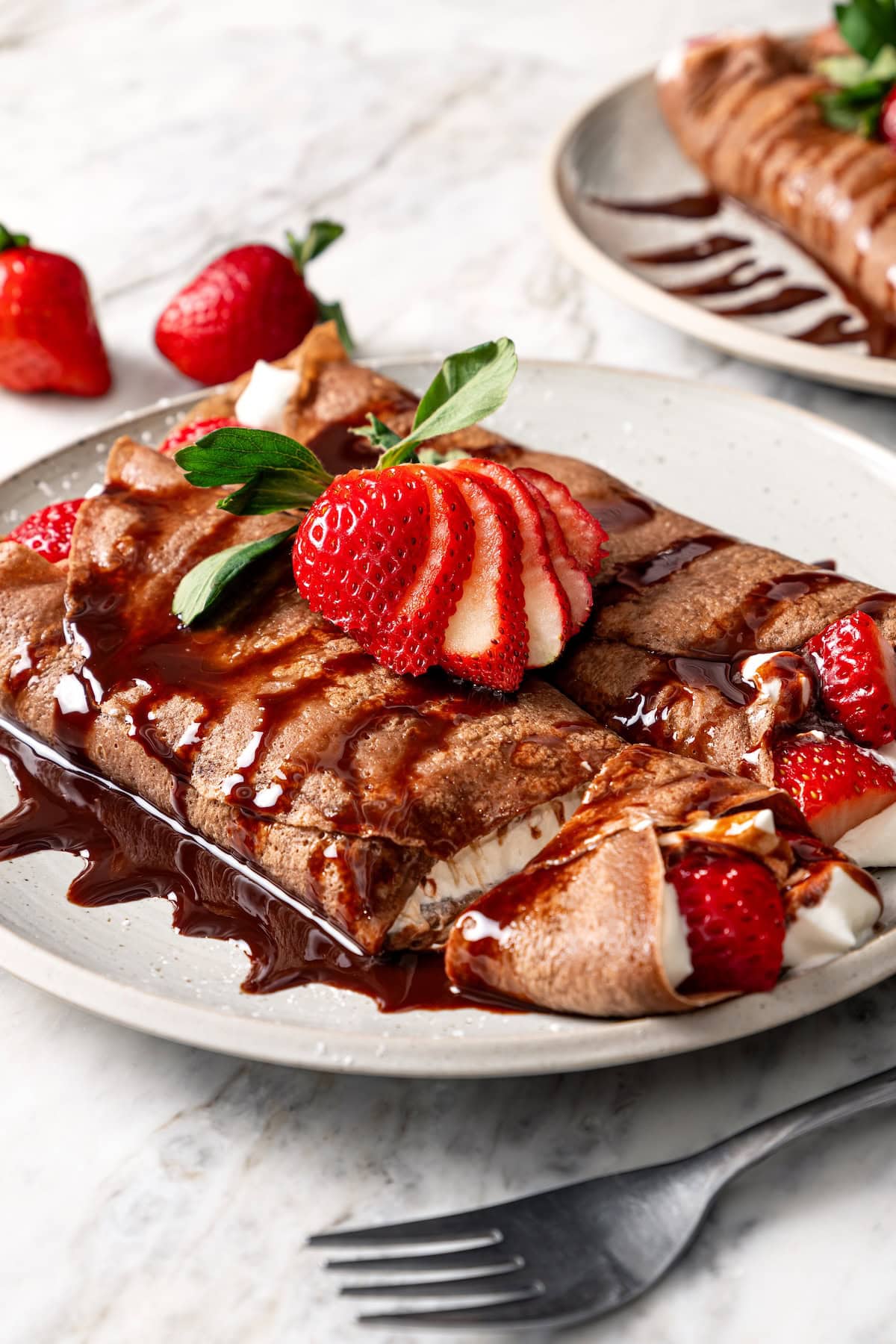 These chocolate crepes are thin, tender and lightly sweet, filled with strawberries and whipped topping. Serve them for breakfast or dessert! Two chocolate crepes filled with whipped cream and strawberries.