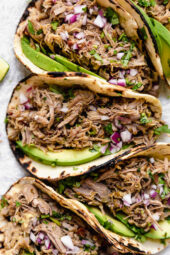 Slow cooker carnitas tacos with avocado slices.