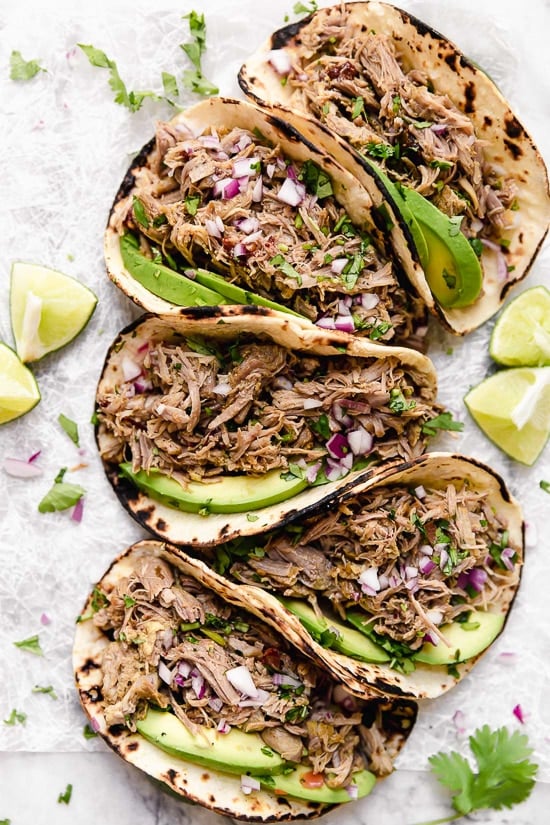 Slow cooked until tender then crisped in the oven, these pork carnitas are practically effortless to make and perfect for meal prep. 5 pork carnitas tacos topped with slices of avocado and red onion.