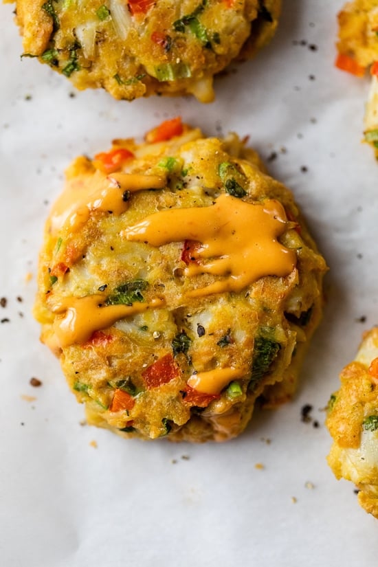 This easy baked crab cakes recipe combines juicy lump crab meat, simple seasonings, and fresh herbs. Perfect as an appetizer or light dinner! Close up of a baked lump crab cake drizzled with red pepper sauce.