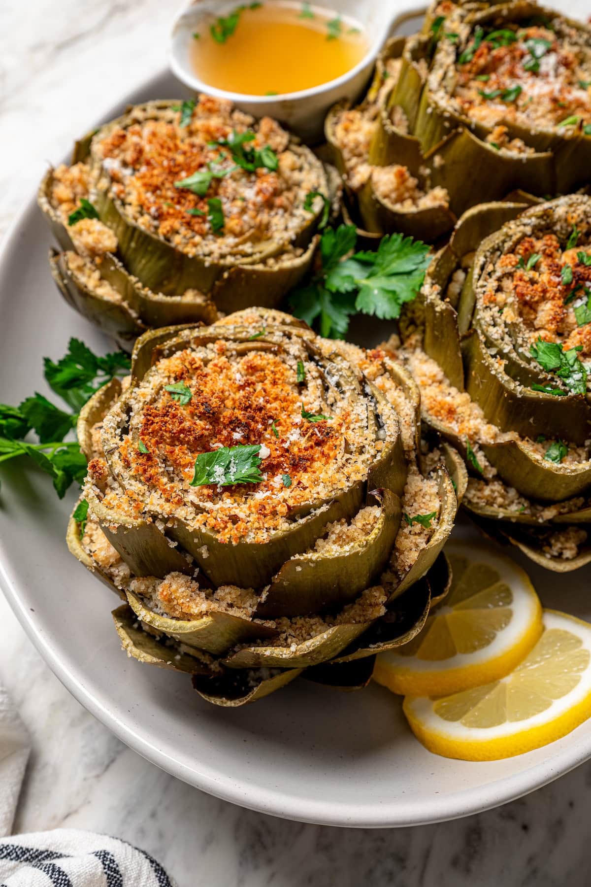 Stuffed artichokes are a classic Italian dish made with crispy, cheesy breadcrumbs. My version is a bit lighter but just as delicious! Platter of stuffed artichokes with sliced lemon
