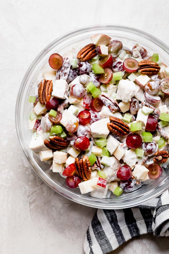 This lightened up chicken Waldorf salad is creamy and crisp, with tender chicken, apples, grapes, celery and nuts in a light dressing. Creamy chicken Waldorf salad in glass mixing bowl.