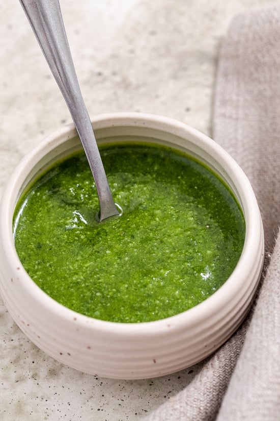This fresh basil pesto is made with basil, garlic and Parmesan. Leaving out the pine nuts and reducing the olive oil makes it lighter! Homemade Basil Pesto in bowl with spoon