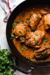 Overhead view of boneless chicken thighs in a skillet with shallots in wine sauce with red wine vinegar.