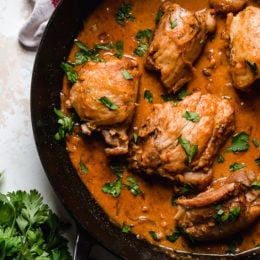 Overhead view of boneless chicken thighs in a skillet with shallots in wine sauce with red wine vinegar.