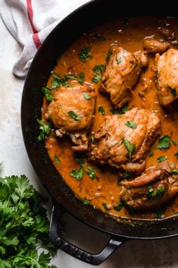 Overhead view of boneless chicken thighs in a skillet with shallots in wine sauce with red wine vinegar.