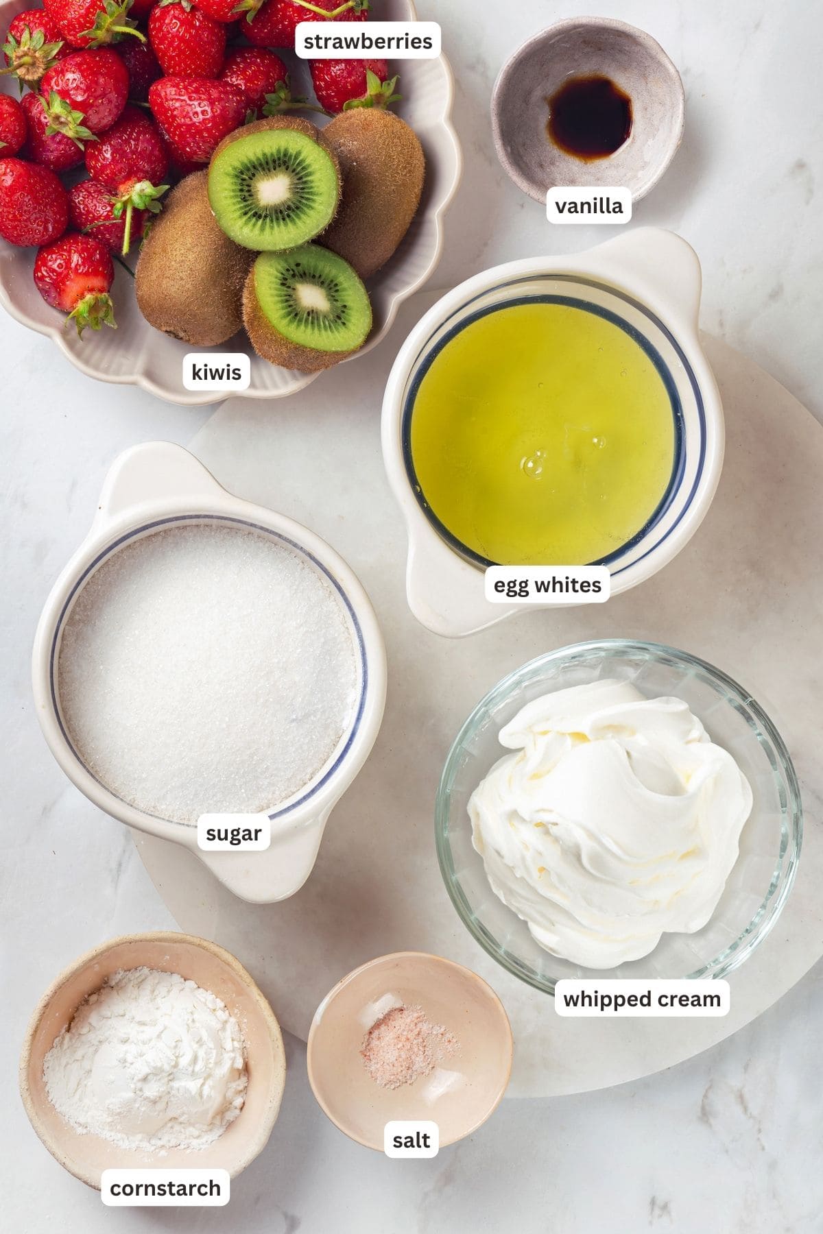 Pavlova is an elegant, light dessert that pairs airy meringue nests with whipped cream and fresh fruit. It's almost too pretty to eat! Overhead view of ingredients for pavlova with labels