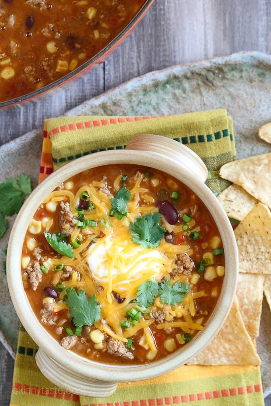 Loaded with beans, ground turkey, tomatoes, and corn, this Easy Taco Soup is hearty, filling, and ready in just 20 minutes! Overhead view of a bowl of turkey taco soup with sour cream, cheese, and cilantro.