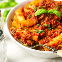 A bowl with sausage pasta sauce served over rigatoni.