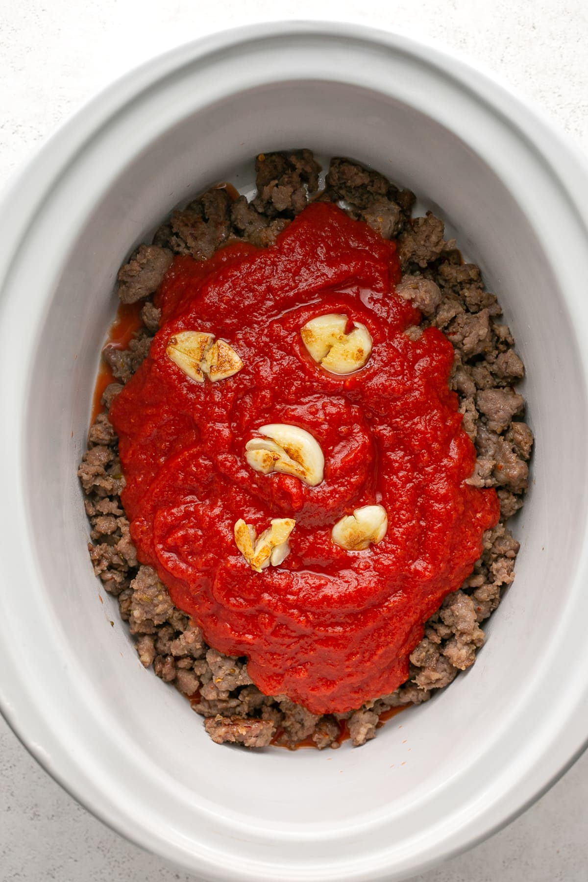 This easy, 5-ingredient sausage pasta sauce is made in the crock pot with flavorful chicken or turkey Italian sausage. Perfect for weeknights! Crushed tomatoes and garlic added to ground sausage in the crock pot.