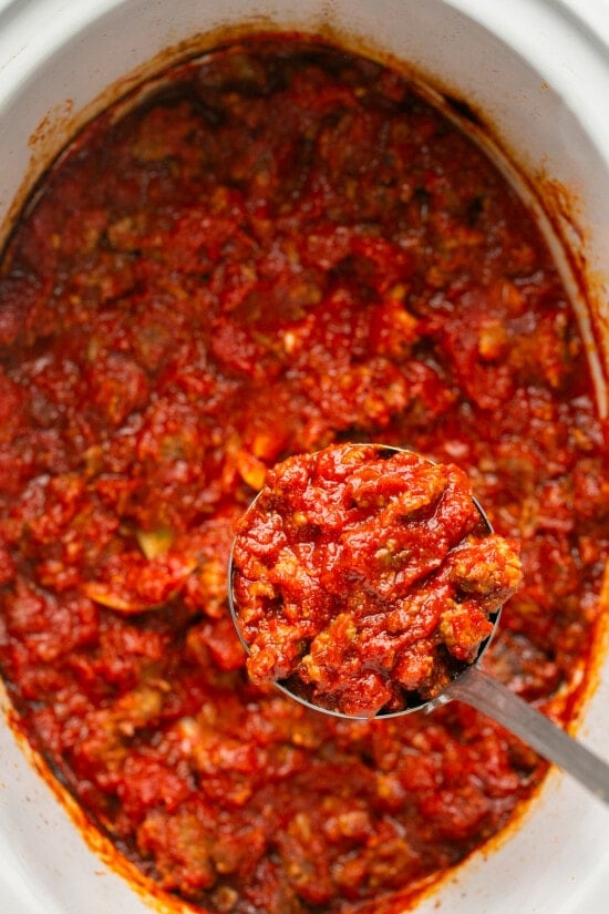 This easy, 5-ingredient sausage pasta sauce is made in the crock pot with flavorful chicken or turkey Italian sausage. Perfect for weeknights! A spoon lifting sausage pasta sauce from a crock pot.