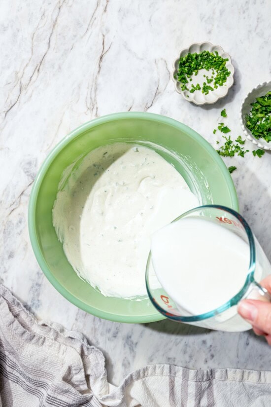 This lightened-up buttermilk ranch dressing is creamy, tangy, and full of fresh herbs. It’s an easy, lighter take on a classic favorite. Pouring buttermilk into bowl for ranch dressing.