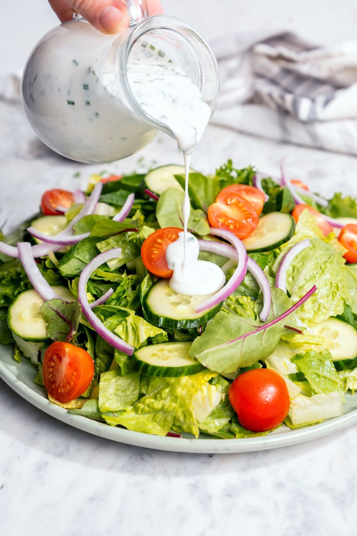 This lightened-up buttermilk ranch dressing is creamy, tangy, and full of fresh herbs. It’s an easy, lighter take on a classic favorite. Pouring buttermilk ranch dressing onto garden salad.