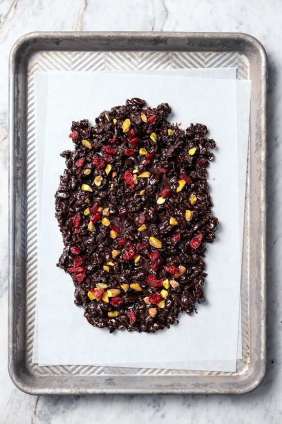 This easy Dark Chocolate Bark with Pistachios and Cranberries is festive enough for a holiday treat, but healthy enough to enjoy year round! Dark chocolate bark with pistachios and cranberries on parchment paper.