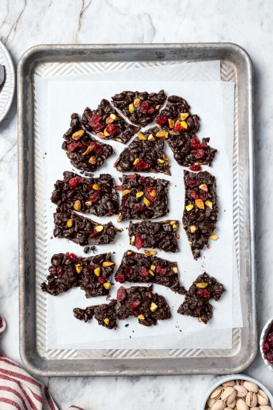 This easy Dark Chocolate Bark with Pistachios and Cranberries is festive enough for a holiday treat, but healthy enough to enjoy year round! Dark chocolate bark broken into pieces on parchment paper.