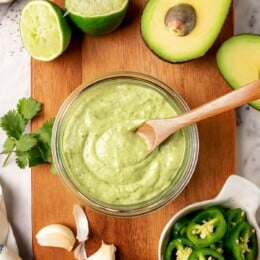 Glass jar of avocado cilantro lime dressing with wooden spoon.