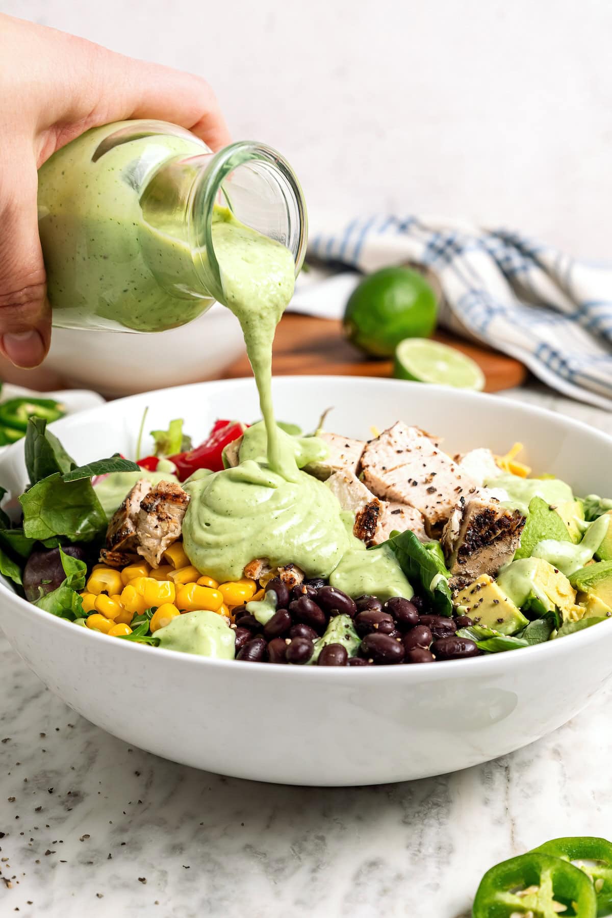 Creamy, bright, and tangy thanks to a buttermilk base, this avocado cilantro lime dressing is perfect for salads, tacos, and dipping veggies. Pouring avocado cilantro lime dressing over salad in bowl.