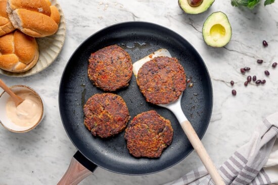 These black bean burgers are flavorful, satisfying and easy to make ahead. With a smoky chipotle mayo and avocado on top, they're delicious! Spatula lifting black bean burger from pan.