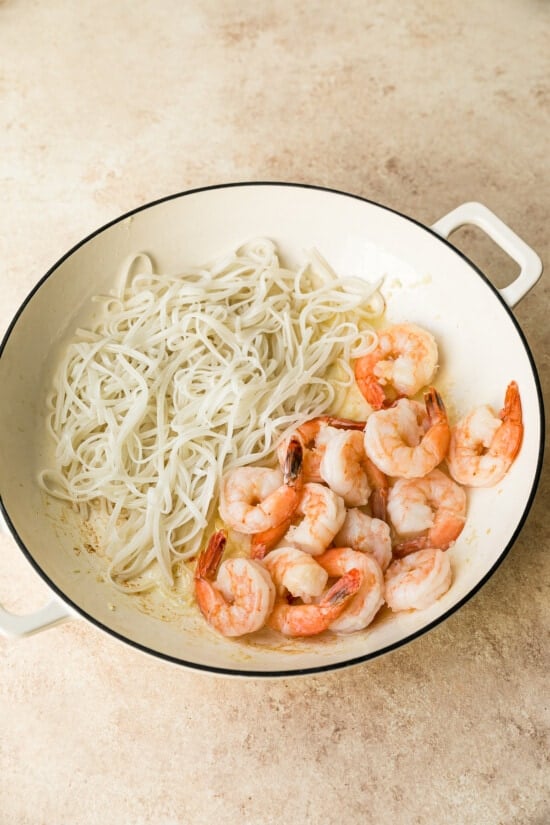 This easy homemade Pad Thai recipe is a lightened up version of the original made with shrimp, eggs, and tofu. Dinner’s done in 25 minutes! Noodles on one side of wok with cooked shrimp on other side