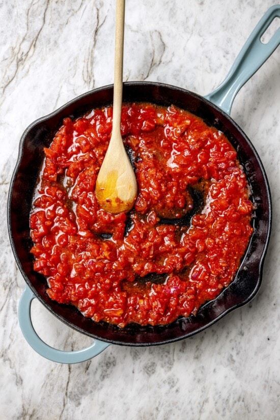 Eggs in purgatory is a simple Italian dish that simmers eggs in a fiery tomato sauce. My version is made with harissa for extra flavor! Stirring sauce for eggs in purgatory