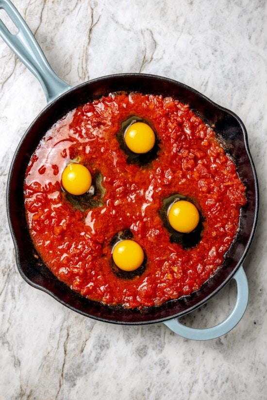 Eggs in purgatory is a simple Italian dish that simmers eggs in a fiery tomato sauce. My version is made with harissa for extra flavor! Eggs cracked into tomato sauce in skillet