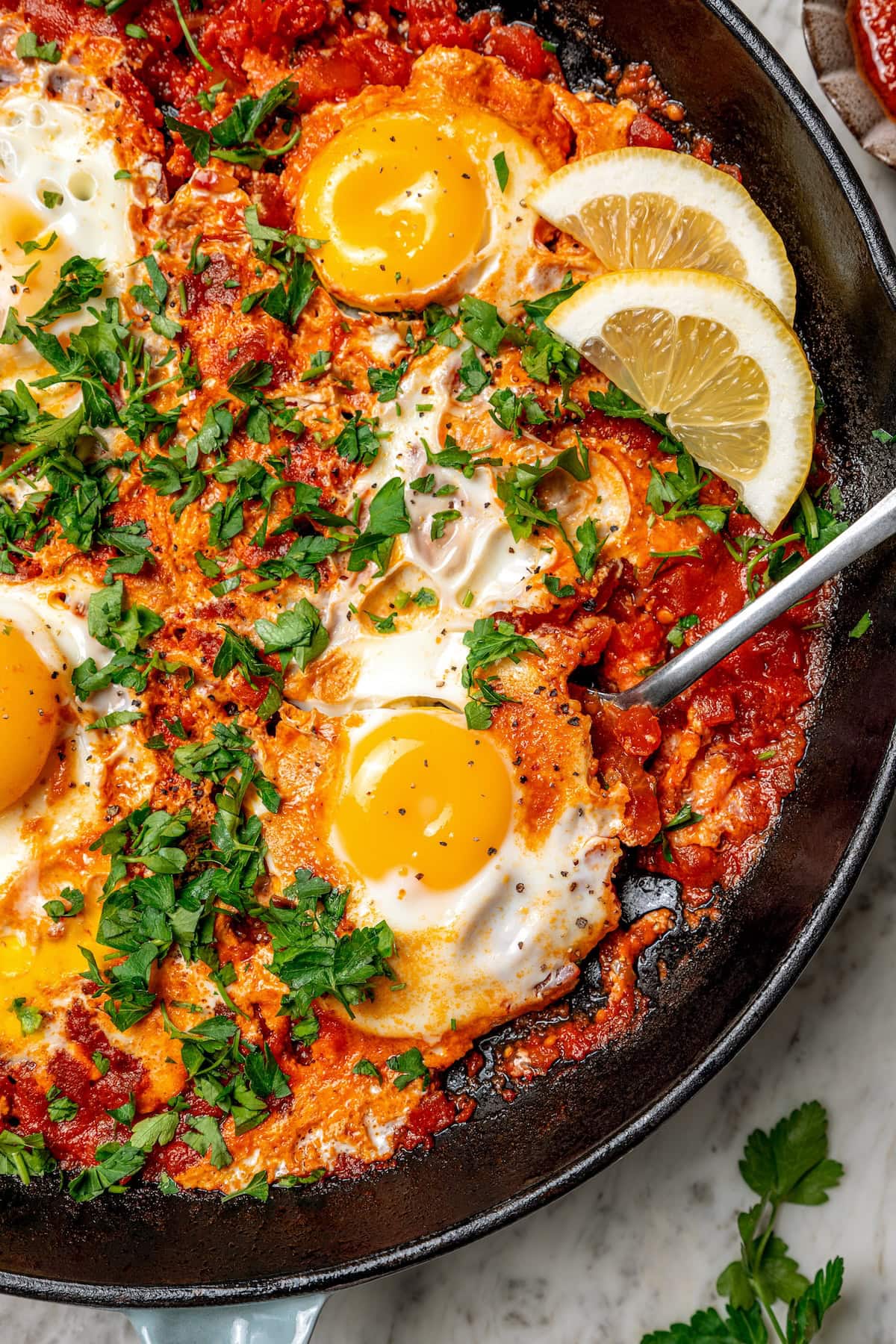 Eggs in purgatory is a simple Italian dish that simmers eggs in a fiery tomato sauce. My version is made with harissa for extra flavor! Overhead view of eggs in purgatory in skillet with spoon