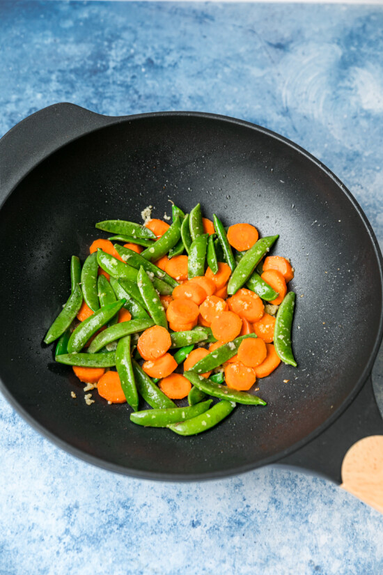 This chicken and vegetable stir fry with snap peas and carrots is sautéed with ginger, lime, and soy sauce. Great for a quick weeknight meal! Snap peas and carrots sautéed with ginger and garlic in a wok.
