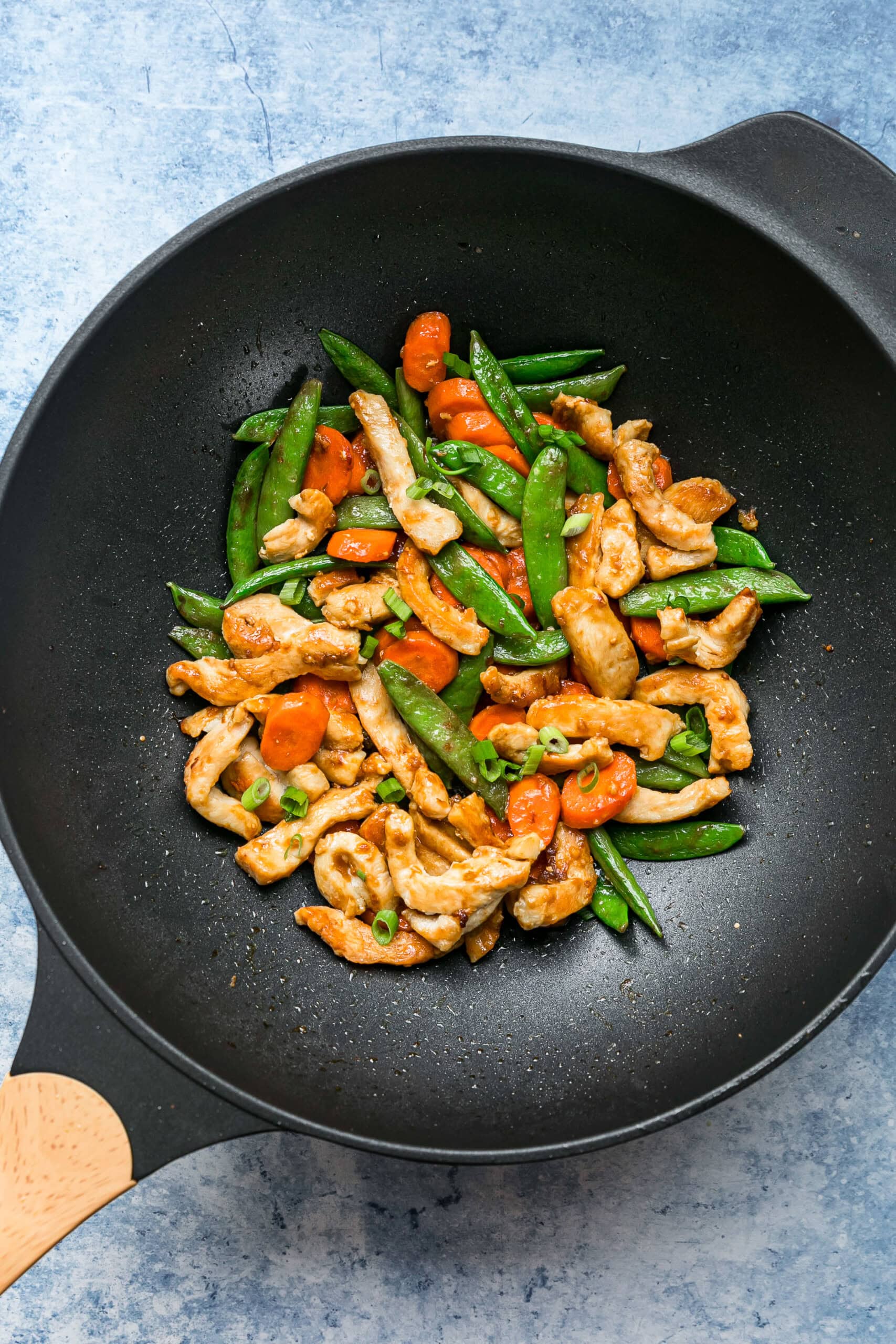 This chicken and vegetable stir fry with snap peas and carrots is sautéed with ginger, lime, and soy sauce. Great for a quick weeknight meal! Overhead view of chicken and vegetable stir fry in a wok.