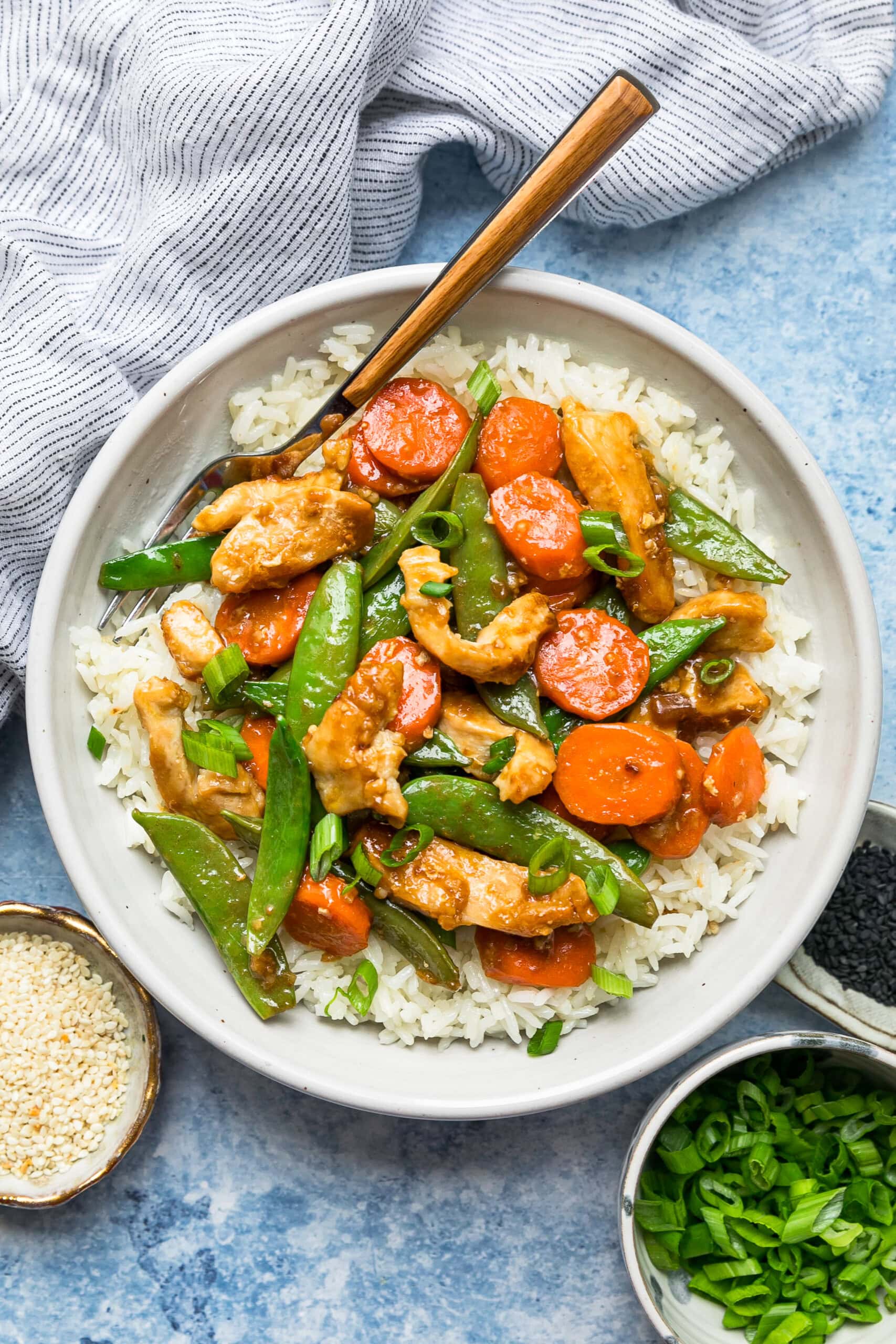 This chicken and vegetable stir fry with snap peas and carrots is sautéed with ginger, lime, and soy sauce. Great for a quick weeknight meal! Overhead view of chicken and vegetable stir fry served over a bowl of rice.