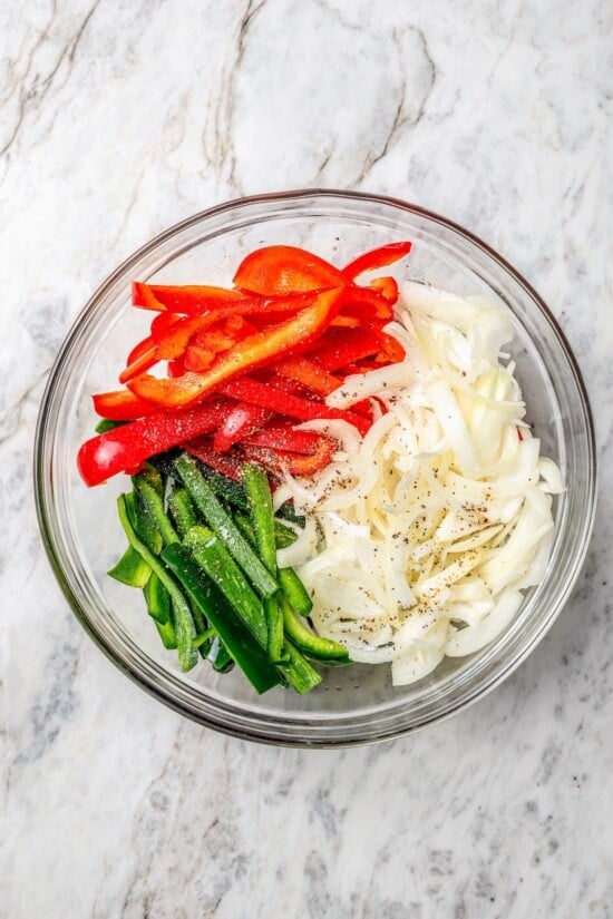 These easy chicken fajitas are made with grilled chicken breast, bell peppers and onions and served sizzling hot with tortillas and cheese! Overhead view of seasoned red peppers, poblanos, and onions in bowl