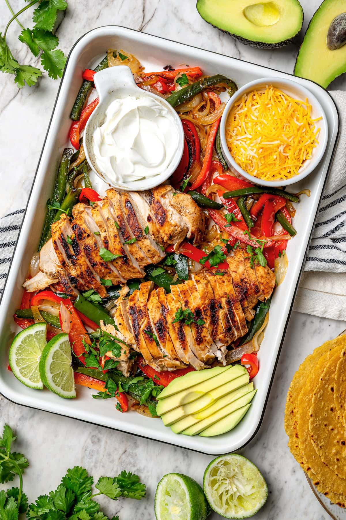 These easy chicken fajitas are made with grilled chicken breast, bell peppers and onions and served sizzling hot with tortillas and cheese! Overhead view of chicken fajitas in pan with bowls of sour cream and cheese