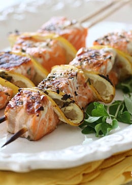 Two grilled salmon kebabs with lemon on a white plate.