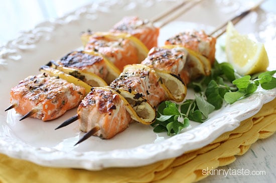 These grilled salmon kebabs are delicious and easy to make with fresh herbs, lemon, and spices. Flavorful, juicy, and perfect for summer! Two grilled salmon kebabs with lemon on a white plate.
