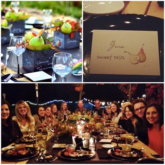 A tabletop with decorative boxes with pears and wine glasses, a name card for Gina from SkinnyTaste with a picture of pears, a group of 14 people around a large dinner table with plates of food and beverages